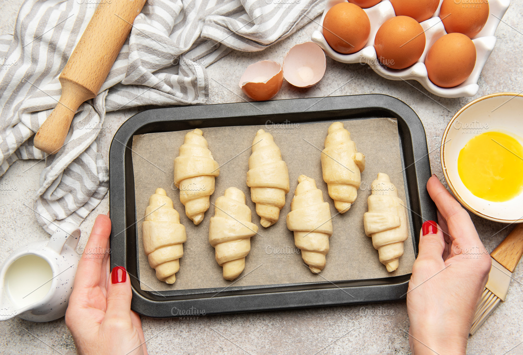 Baker placing tray of raw croissants on table before baking, a Food & Drink Photo by Olena Rudo
