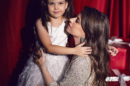 beautiful young woman in a shiny dress is sitting with a daughter child on red, a Person Photo by SaulichPhoto