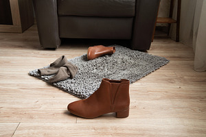 Brown leather ankle boot on floor near rug in home interior, an Industrial Photo by MDBildes