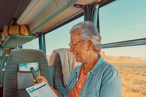 Senior woman sitting by the window inside a moving coach bus, a Person Photo by DanFLCreativo