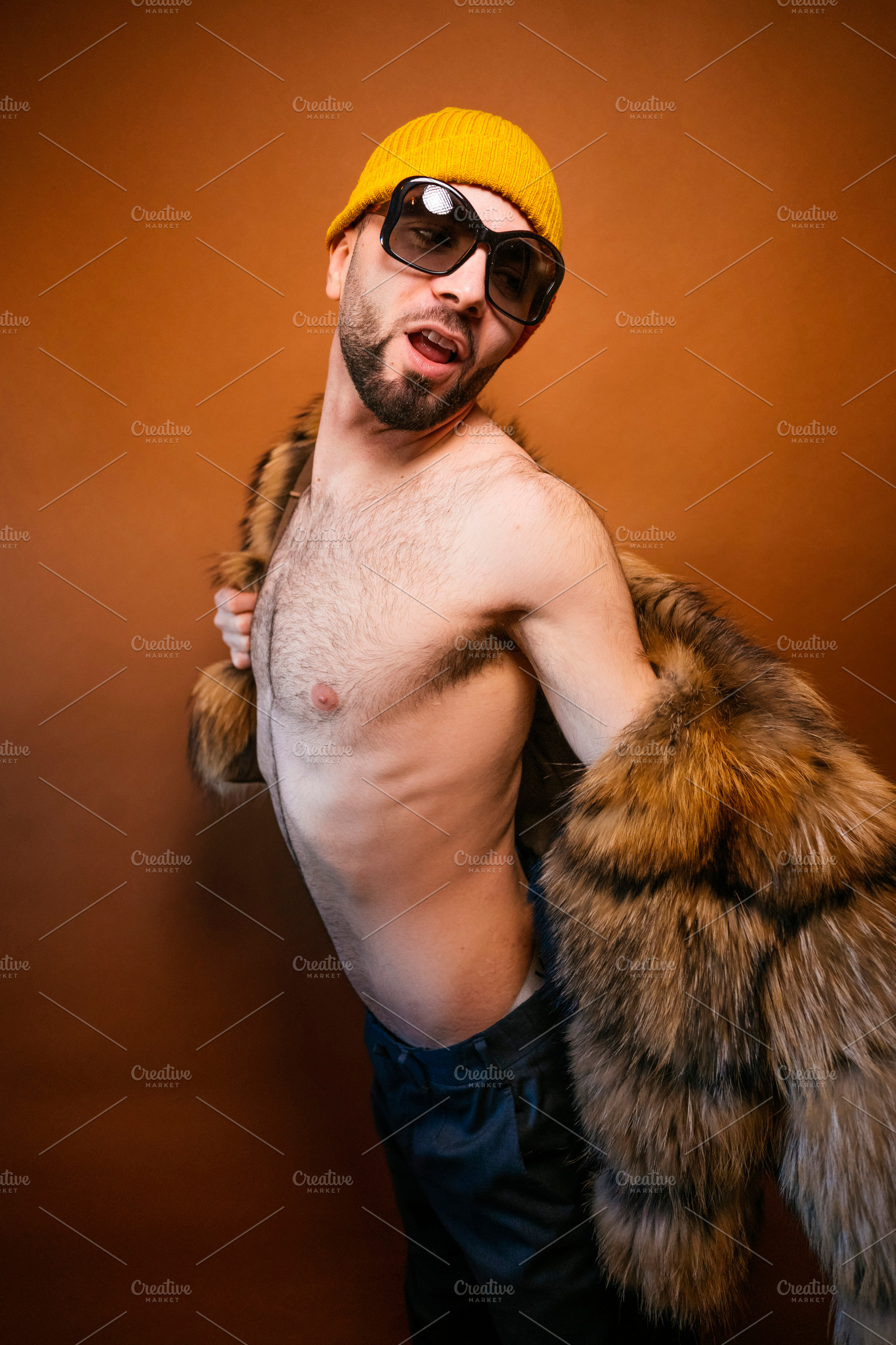 Confident man posing shirtless with fur coat and beanie, a Photo by karrastock
