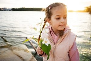 Young girl holding flowers by a lake during a peaceful sunset moment, a Photo by AS photostudio