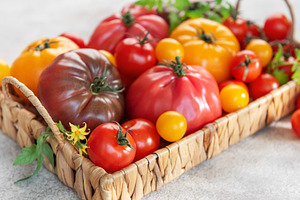 Fresh organic heirloom tomatoes in a woven basket, a Food & Drink Photo by Olena Rudo