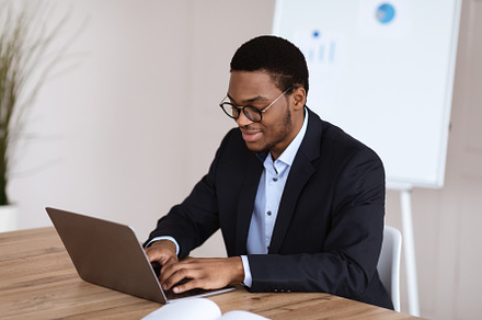 Young black manager smiling while working with laptop, office interior, a Photo by Prostock-Studio