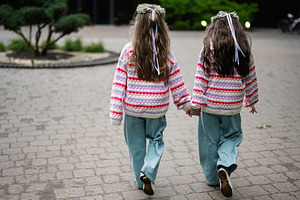 Two children holding hands dressed in colorful sweaters, walking outdoors toget, a Photo by AS photostudio