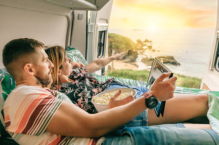 Couple watching a movie on the tablet eating popcorn lying on the bed of their, a Holiday Photo by davidpereiras