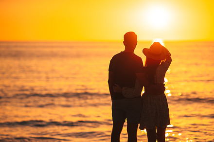 Romantic couple on the beach at colorful sunset on background, a Person Photo by travnikovstudio