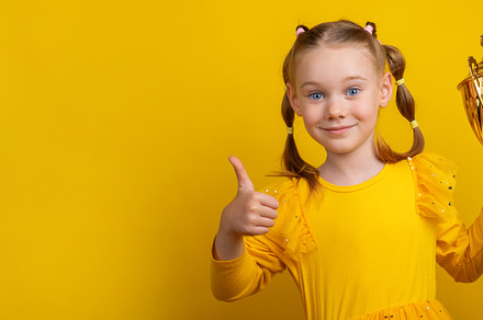 Smiling girl in yellow dress showing thumbs up and holding golde