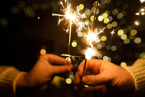 Hands holding fireworks against christmas tree lights bokeh in e, a Holiday Photo by Sonjachni