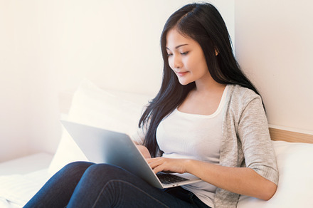 Young woman working on a laptop sitting on bed at home, a Person Photo by Casanowe-studio