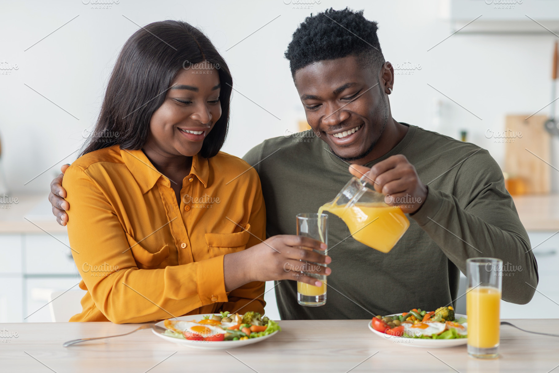 Happy young black spouses having breakfast together, husband pouring juice from, a Photo by Prostock-Studio