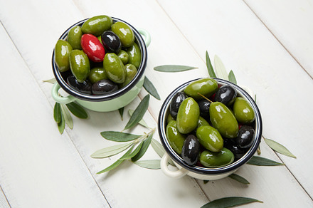 Mixed olives in small bowls on white planks background