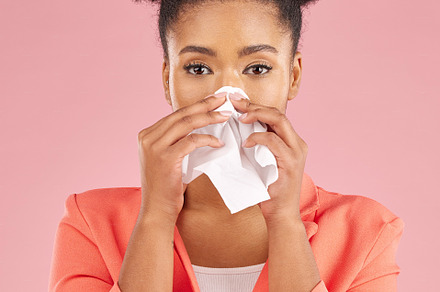Woman, tissue and sneeze in studio portrait for healthcare, hygiene and allergy by pink background. African gen z girl, sick student or model with toilet paper, blowing nose or cleaning for self care, a Photo by Peopleimages.com