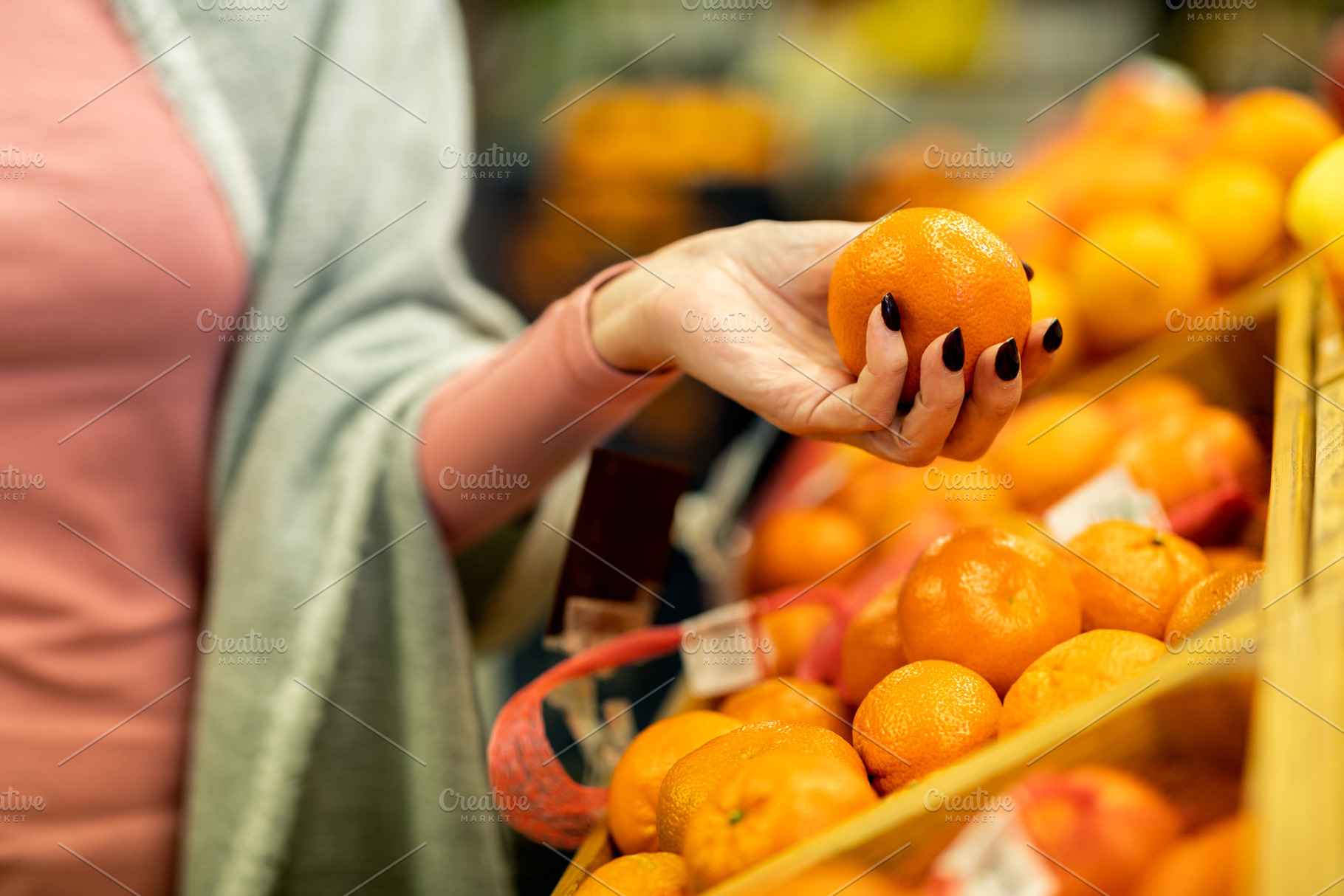 Cropped of woman shopping at supermarket, choosing tangerine, a Photo by Prostock-Studio