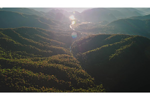 Sun shining over forested mountains, a Nature Photo by Goinyk