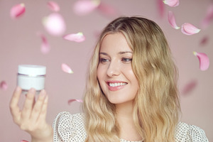 Young woman smiling, holding a skin cream jar. Pink petals falli, a Person Photo by Studio ANNA