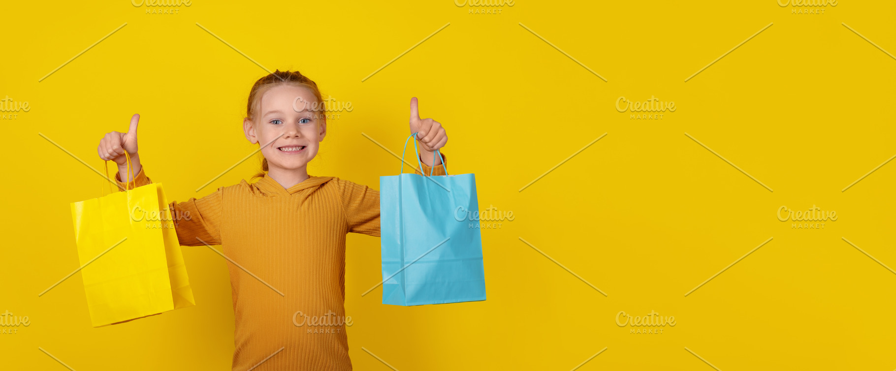 Smiling young girl holding yellow and blue shopping bags, standi, a Person Photo by Ales Munt