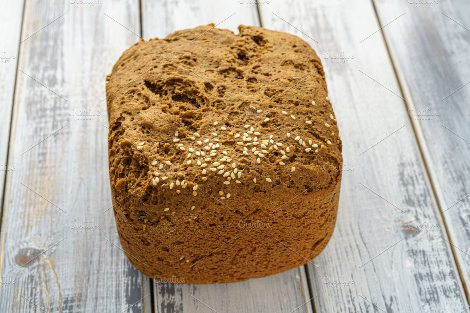 Whole grain bread loaf with sesame seeds and flax seeds on a rustic wooden tabl, a Food & Drink Photo by Eugene_Photo