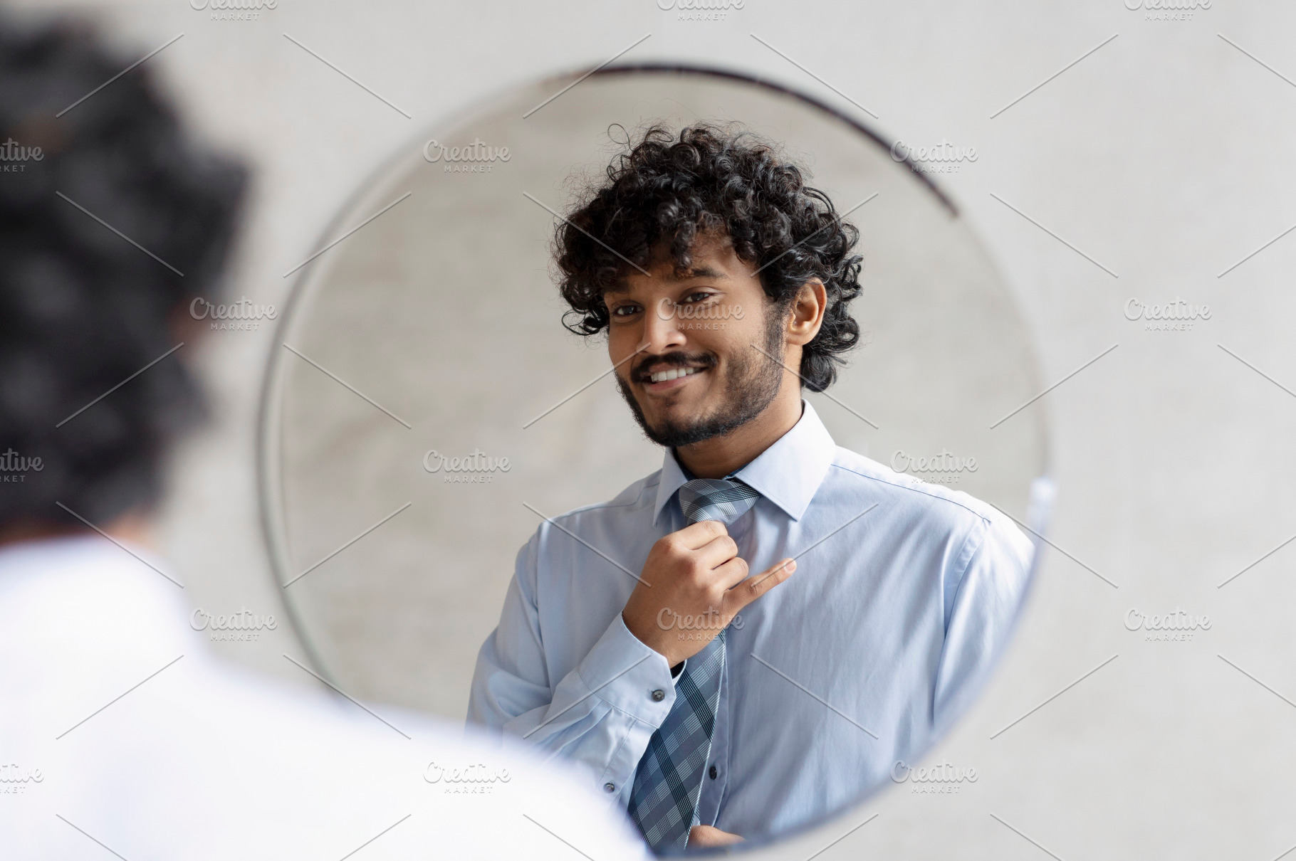 Handsome indian businessman putting on necktie and looking at his reflection in, a Person Photo by Prostock-Studio