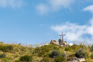 Large metal cross standing on a hilltop under blue sky, a Photo by Antonio Gravante Market