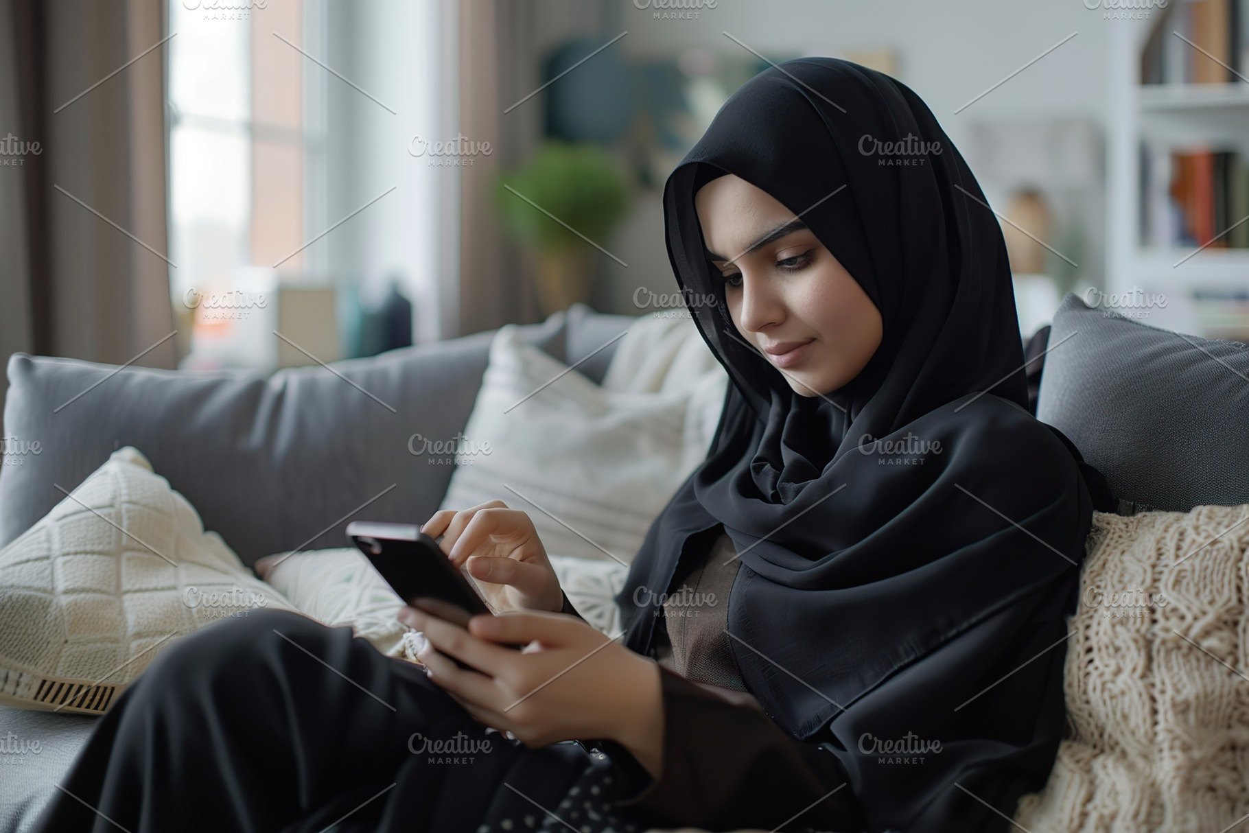 Portrait of young arabian girl in hijab using phone and sitting on sofa. Muslim, a Person Photo by AlyaAnd