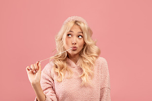 Pretty blonde woman stretching chewing gum from mouth and looking away at free, a Photo by Prostock-Studio