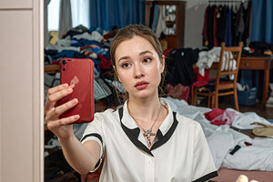Young woman holding a phone takes a mirror selfie in a cluttered, a Person Photo by DanFLCreativo