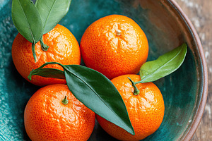 Modern ceramic bowl filled with vibrant oranges and fresh green leaves on woode, a Food & Drink Photo by AlyaAnd