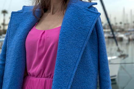 Beautiful woman in pink dress and blue jacket posing on a sailboat in a city ha