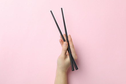 Female hand holding chopsticks on pink background, a Food & Drink Photo by AtlasStudio