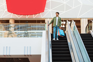 Man Shopping In Mall Holding Bags Standing On Moving Stairs, a Photo by Prostock-Studio