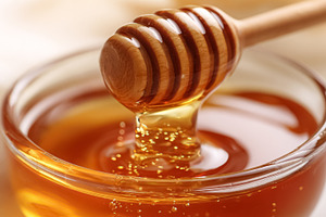 Golden honey dripping from a wooden dipper into a clear glass bo, a Photo by Studio ANNA