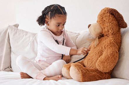 Stethoscope, teddy bear and girl in bed for heartbeat in  hospital doctor or nurse game play of love, support and care. Young child learning, test and check medical heartbeat health exam on baby toy, a Photo by Peopleimages.com
