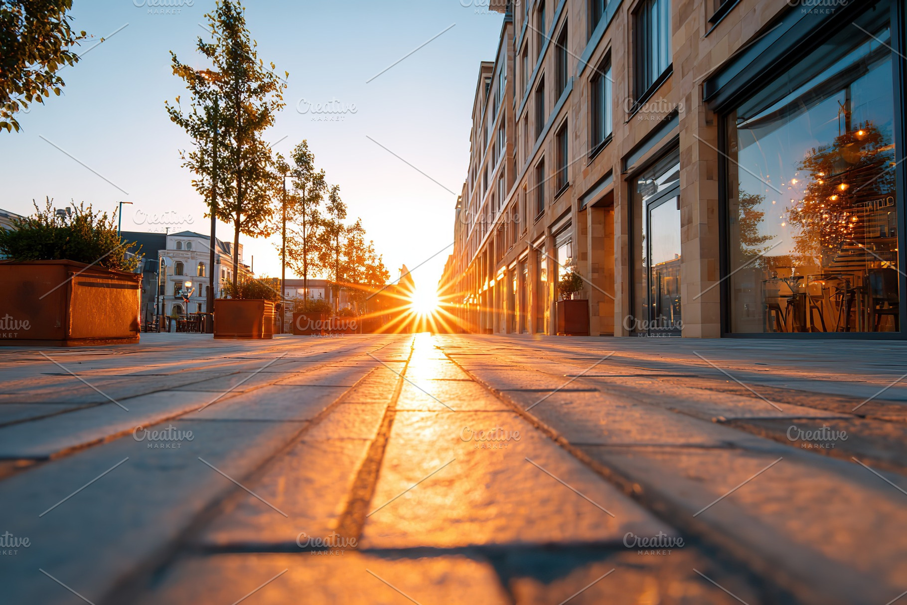Sunset casts golden light on urban street lined with modern buildings and trees, a Photo by AlyaAnd