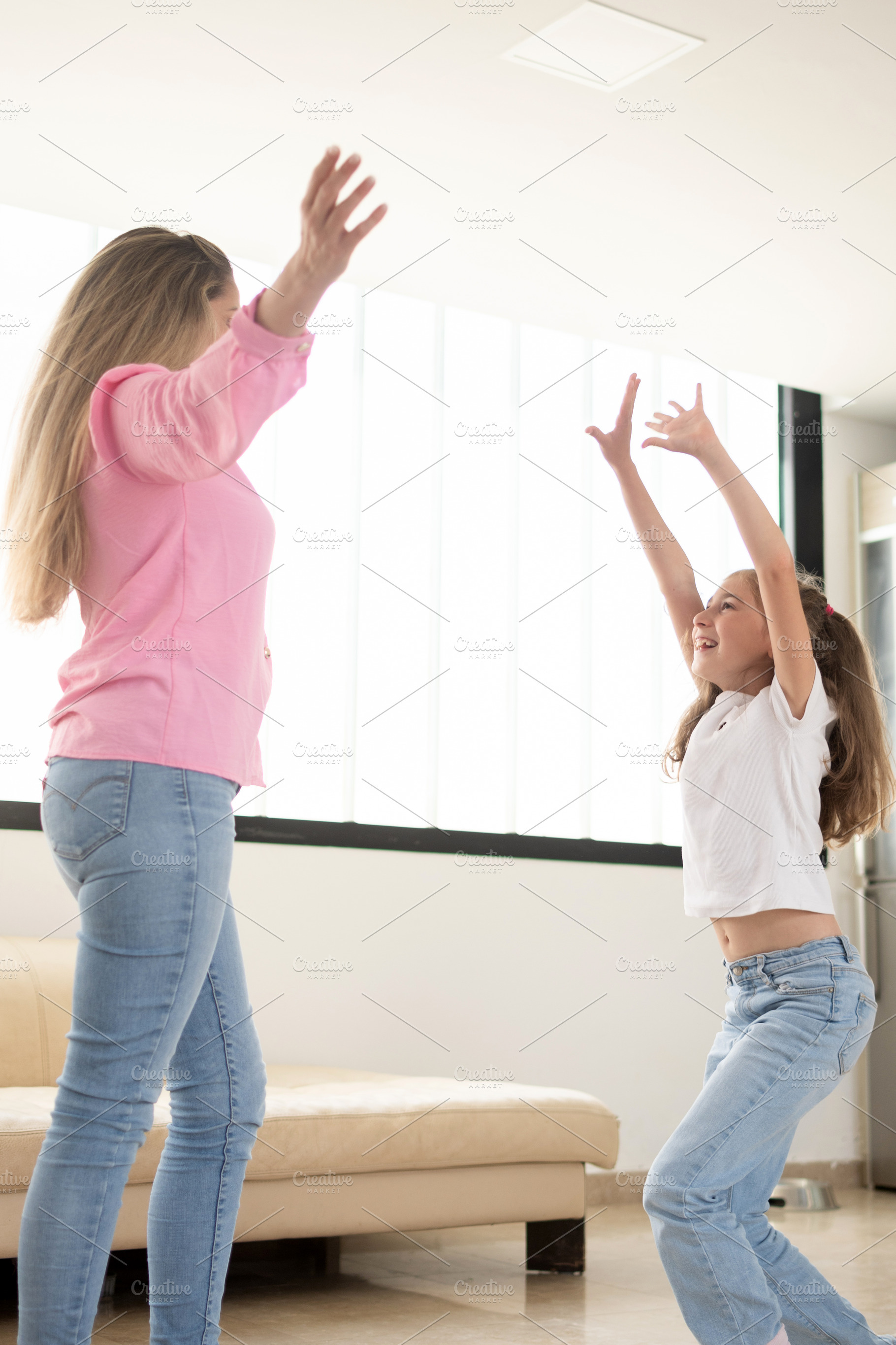 Happy mother and daughter playing together with raised arms at home, a Person Photo by etorres69