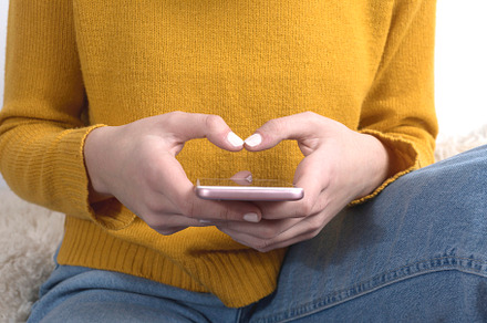 Close up of a woman's hands in yellow sweater using a mobile phone