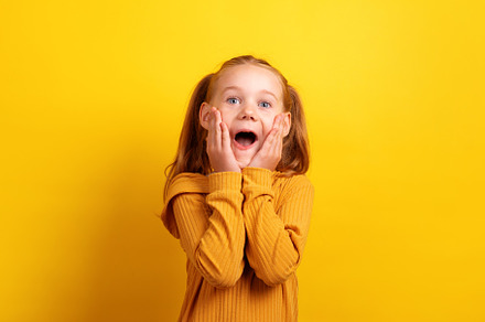 Young girl in mustard sweater showing a surprised expression wit