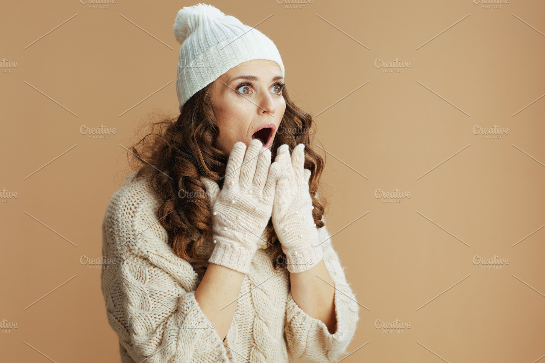 shocked trendy woman in beige sweater, mittens and hat on beige, a Person Photo by Alliance Images