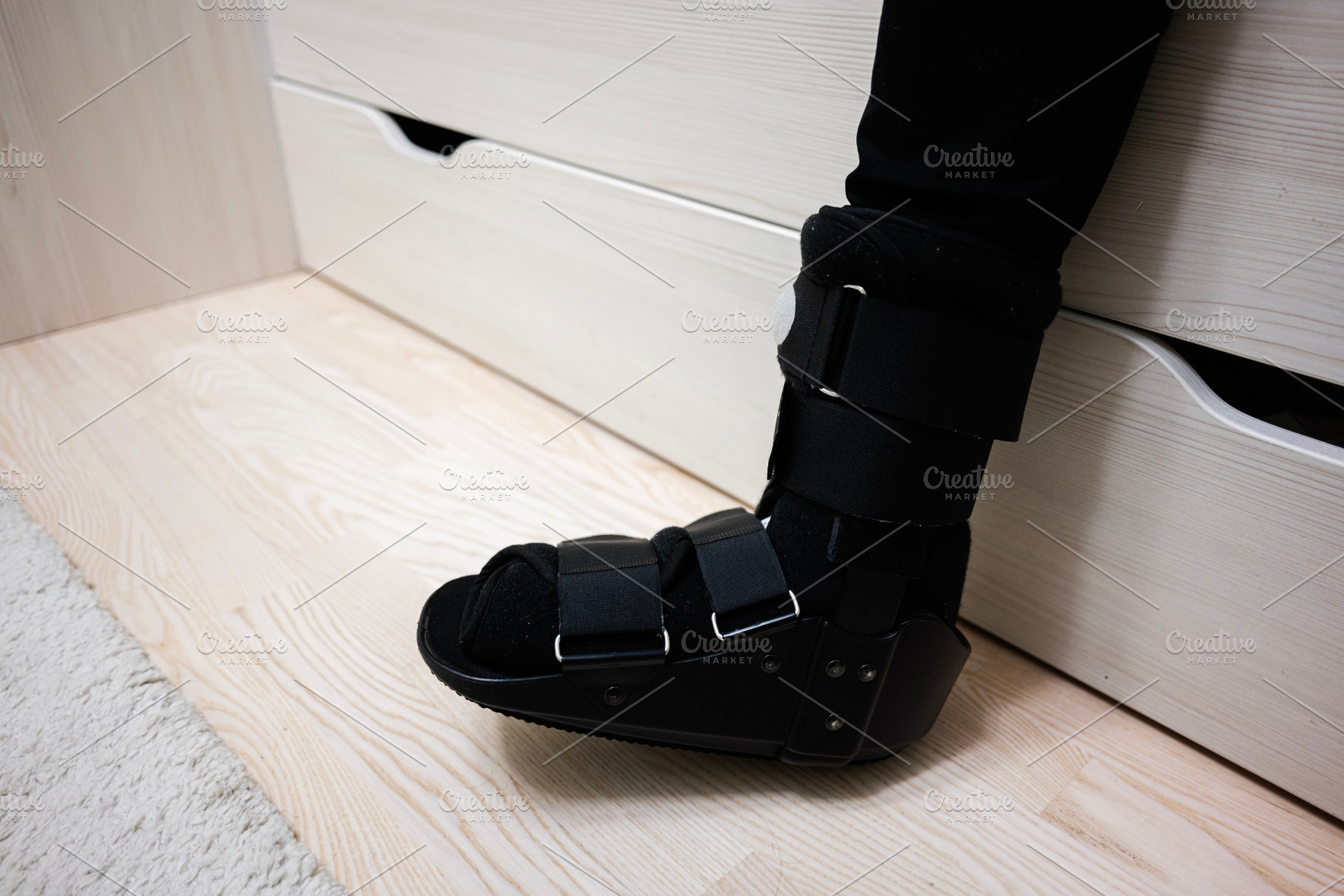 Person wearing orthopedic boot for injury recovery indoors near wooden furnitur, a Health & Medical Photo by AS photostudio
