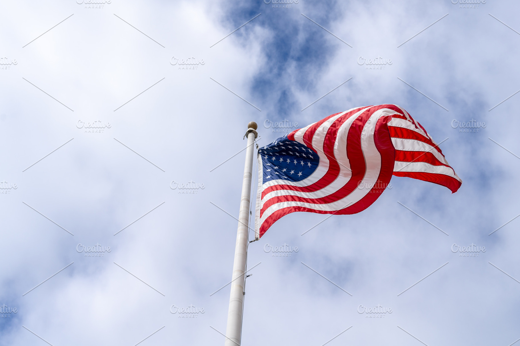 American flag waving on a tall pole against a cloudy sky, a Nature Photo by GoodGoods