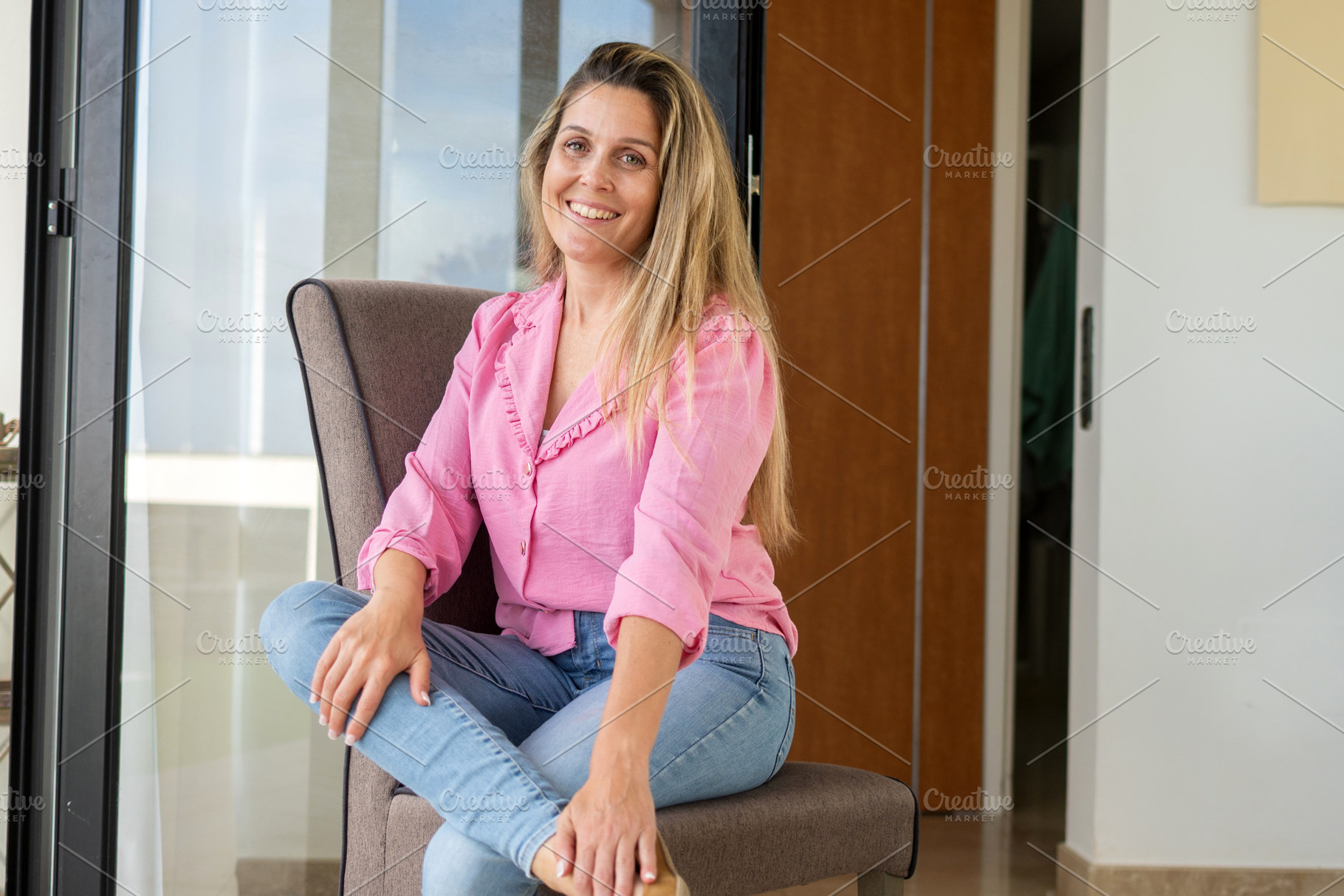 Smiling woman sitting on chair at home looking at camera, a Person Photo by etorres69