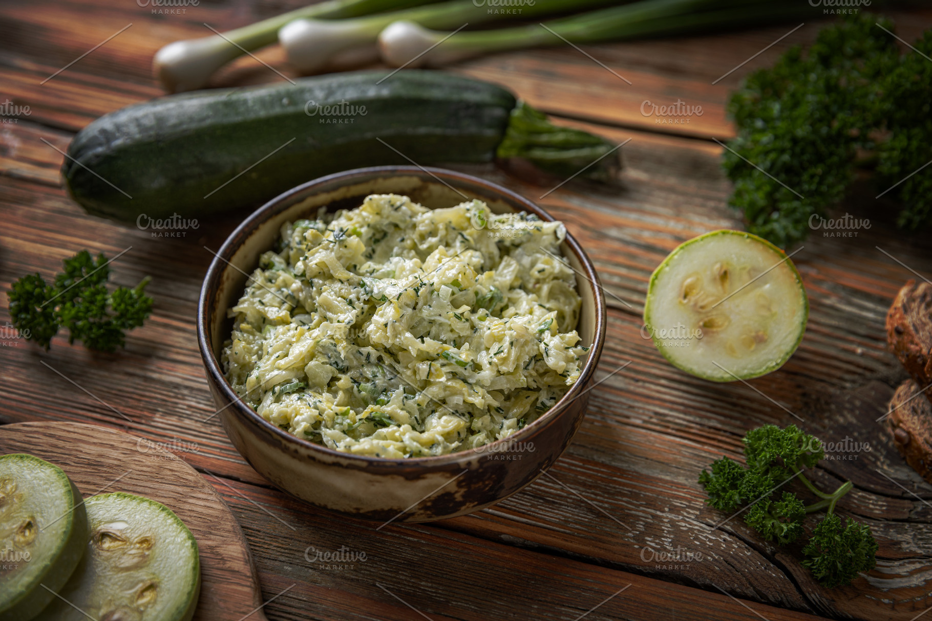 Bowl of zucchini spread is surrounded by fresh zucchini slices,, a Photo by Grafvision photography