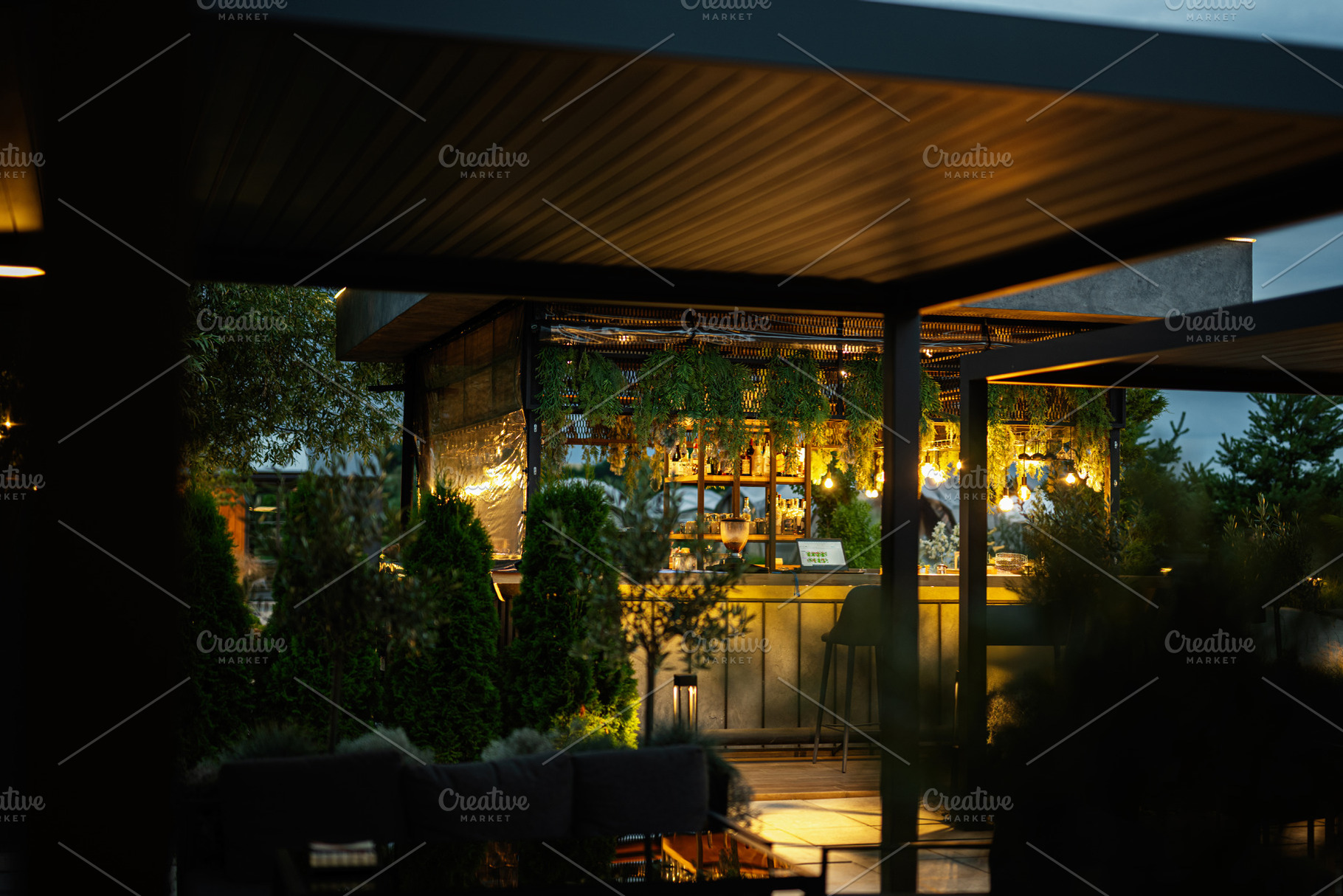 Outdoor rooftop bar with warm lighting surrounded by lush greenery at dusk, a Photo by AS photostudio
