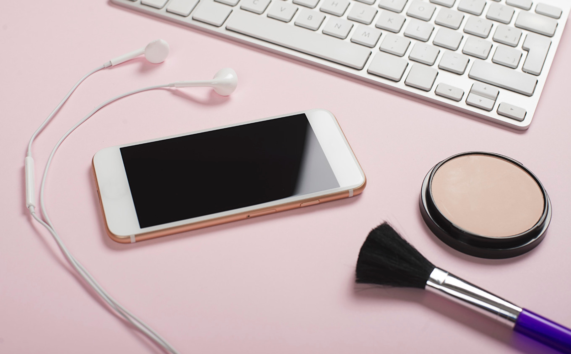 Smartphone headphones and computer keyboard next to makeup on pink and blue, a Technology Photo by José Luis Agudo