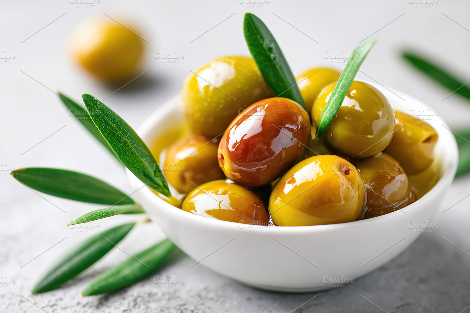 Glossy marinated olives served in a white bowl with fresh olive leaves garnishi, a Photo by AlyaAnd