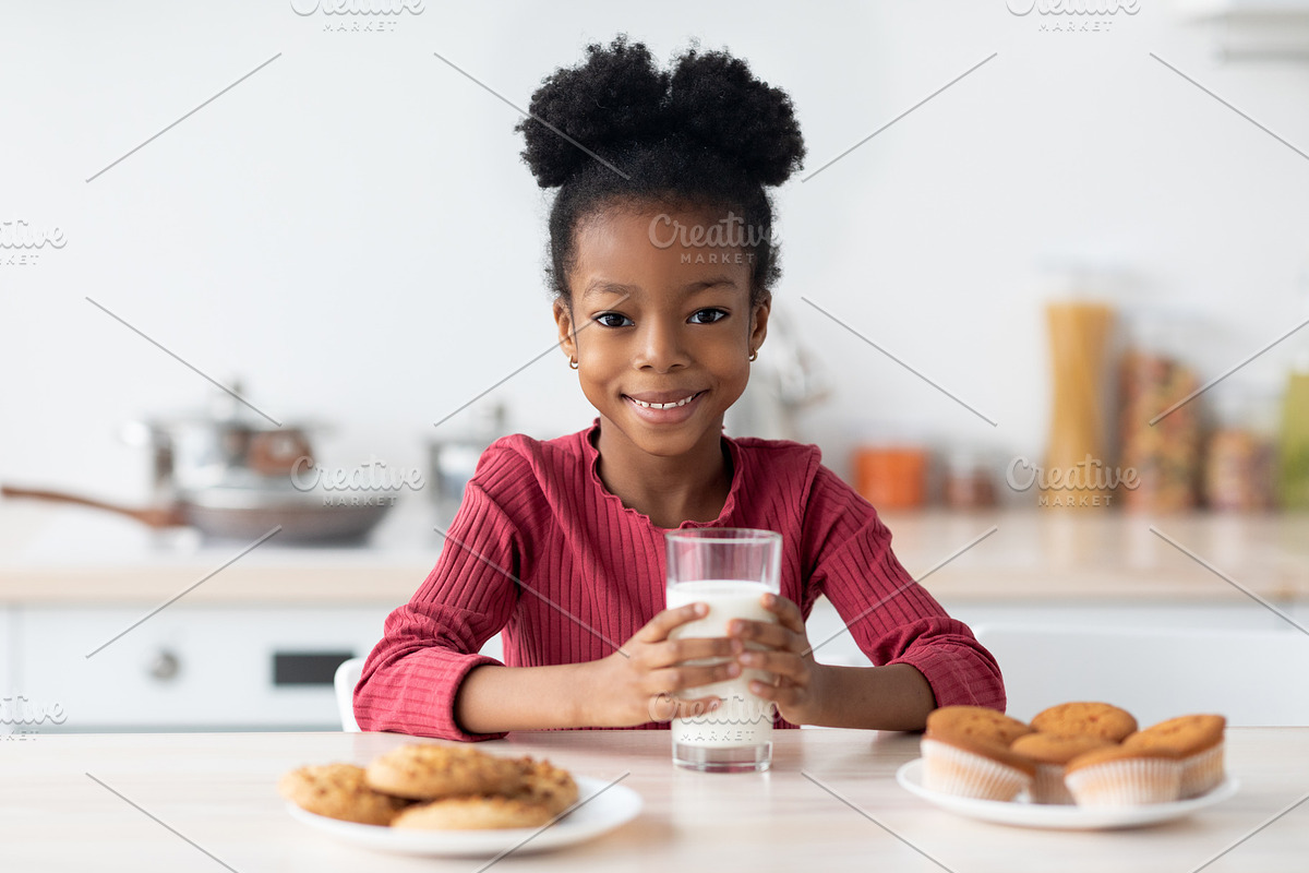 Cheerful Black Girl Sitting At Table, Enjoying Milk And Cookies, a Photo by Prostock-Studio (Photo 1 of 2)