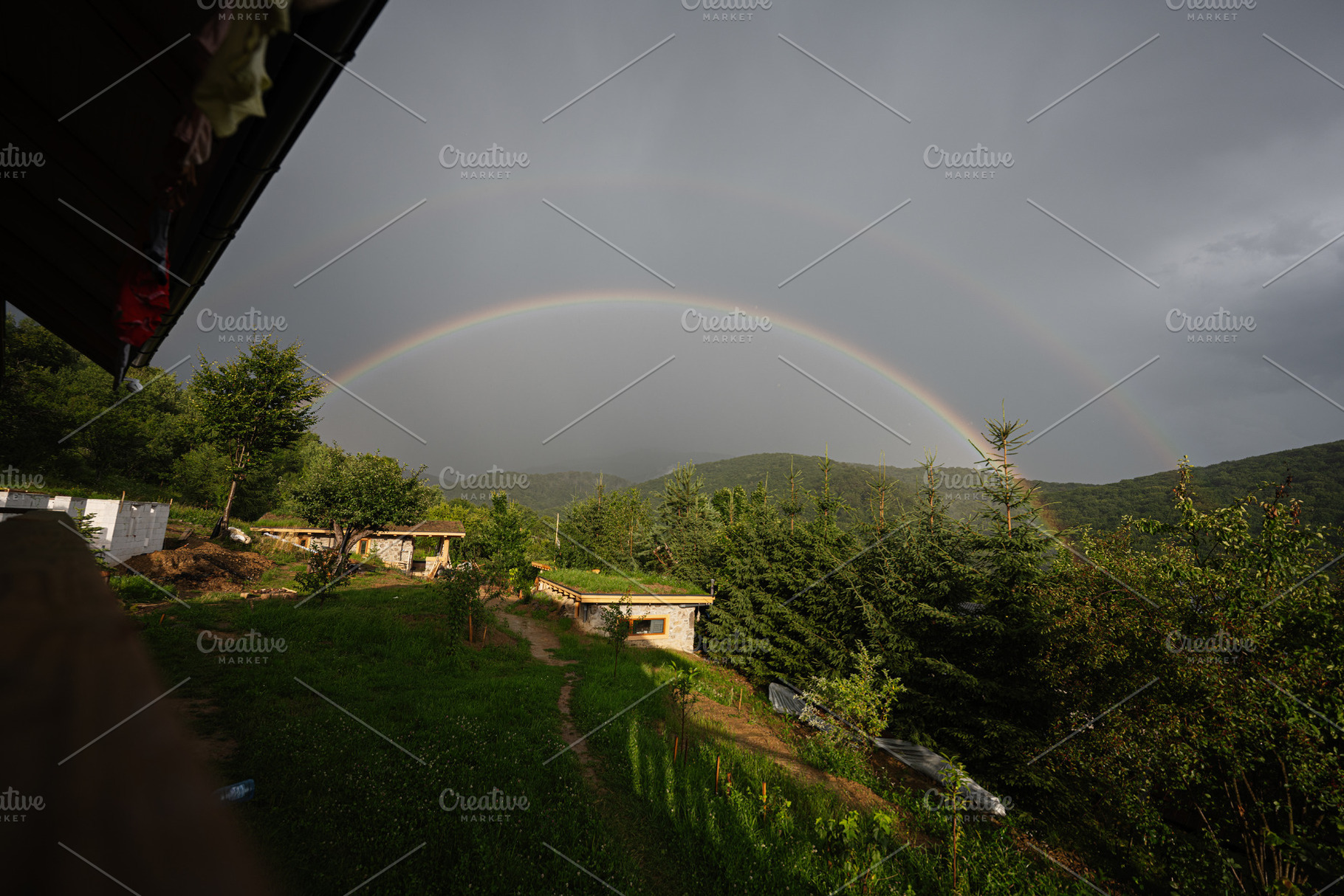 Double rainbow over green forest and houses on a cloudy day, a Photo by AS photostudio