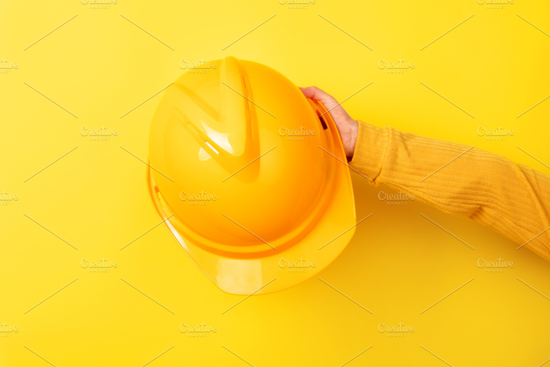 Hand holding a yellow safety helmet against a matching yellow ba, an Industrial Photo by Ales Munt