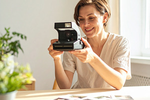 Woman holding analog camara while smiling at looking print photo, a Person Photo by DanFLCreativo