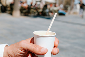 a man holds a cortado in a paper cup, a Photo by Nito